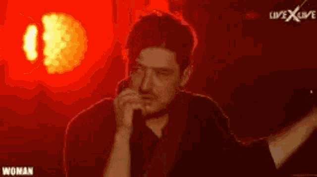 a man is singing into a microphone on stage in front of a red background .