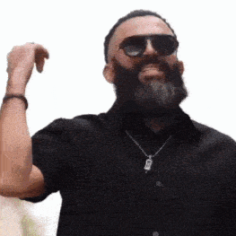 a man with a beard wearing sunglasses and a black shirt is smiling .