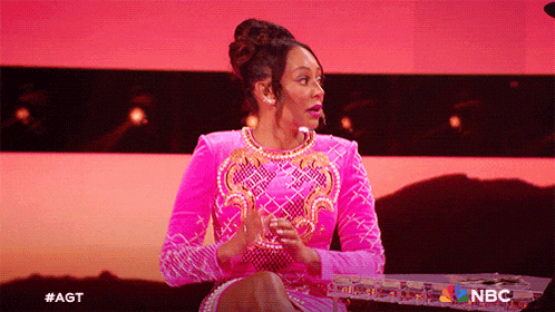 a woman in a pink dress is sitting at a table with the nbc logo on the bottom