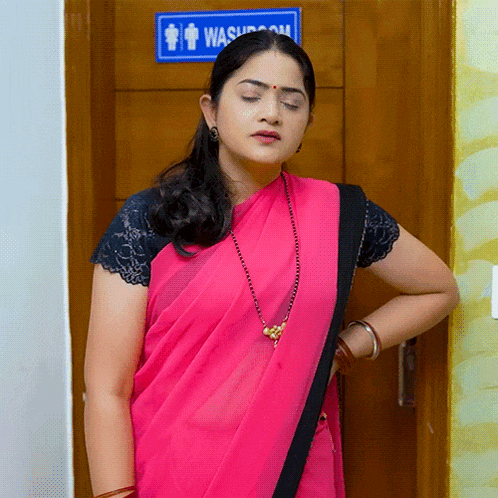 a woman in a pink saree is standing in front of a bathroom sign