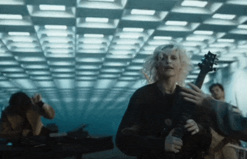 a woman is holding a guitar in a dark room with a ceiling that has a grid pattern .