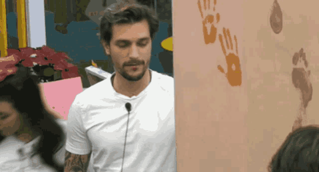 a man in a white t-shirt stands in front of a wall with handprints on it