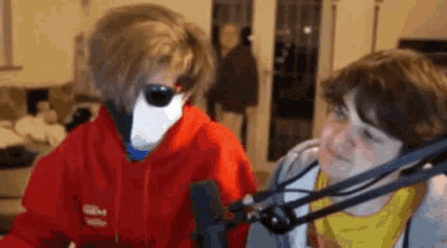 a man in a red hoodie is standing next to another man in a yellow shirt in front of a microphone .