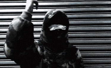 a man wearing a hoodie and sunglasses stands in front of a metal shutter
