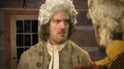 a man in a wig talks to another man