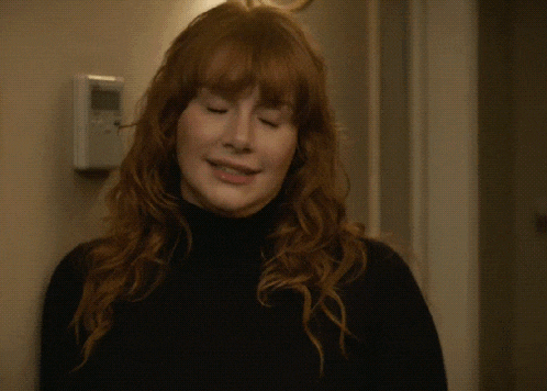 a woman with red hair is waving her hand in front of a door