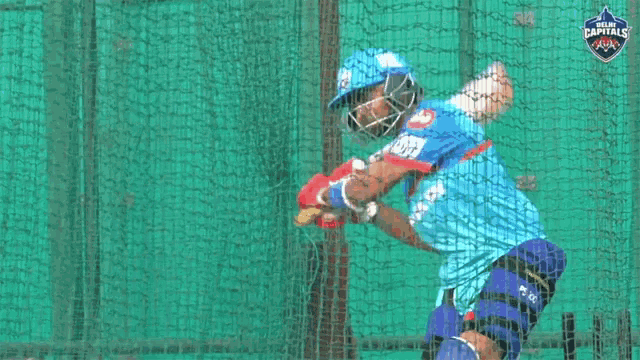 a cricket player is swinging a bat in front of a net with the word capitals on it