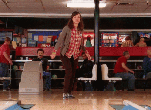 a woman in a plaid shirt is standing on a bowling alley in front of people