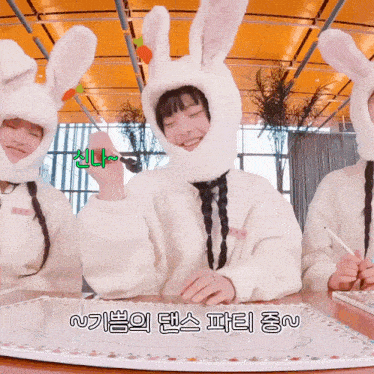three girls wearing bunny hats are sitting at a table in front of a white board with korean writing on it
