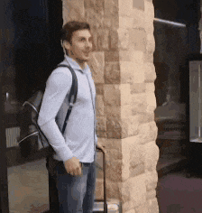 a man standing next to a brick wall with a suitcase