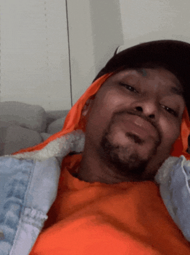 a man wearing an orange shirt and a hat is laying down