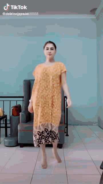 a woman in a yellow dress is dancing in a living room with a chair in the background .