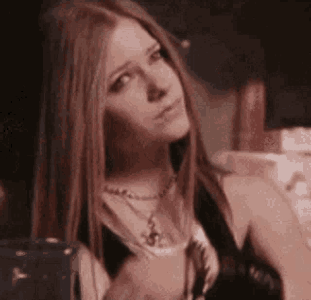 avril lavigne is wearing a black top and a necklace while looking at the camera .