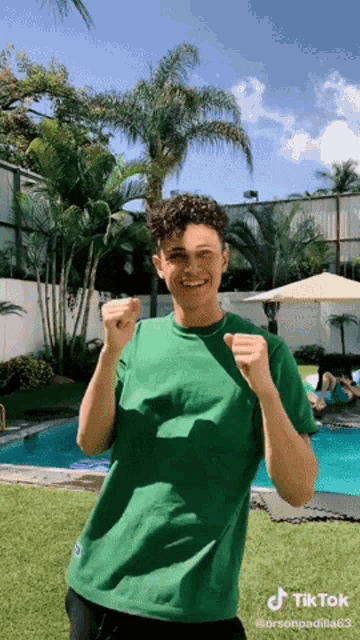 a man in a green shirt is standing in front of a pool with his fist in the air