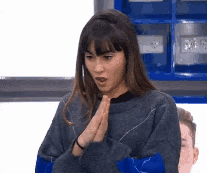 a woman in a gray sweater is making a surprised face while holding her hands together .