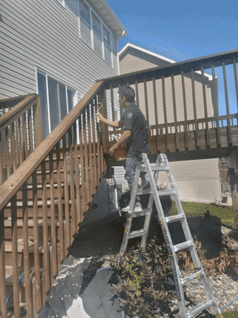 a man on a ladder paints a wooden deck railing