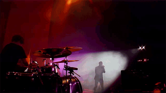 a man stands in front of a drum set and a microphone