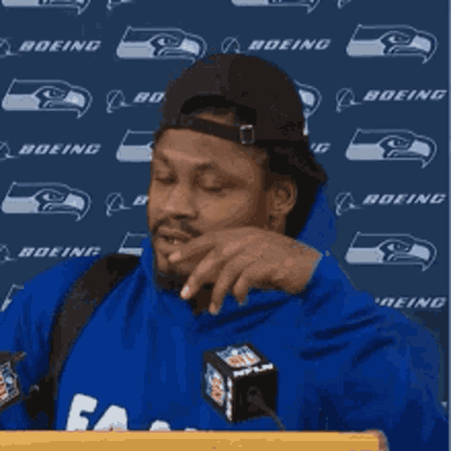 a man wearing a blue hoodie and a black hat stands at a podium