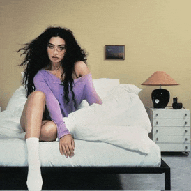 a woman is sitting on a bed wearing a purple sweater and white socks