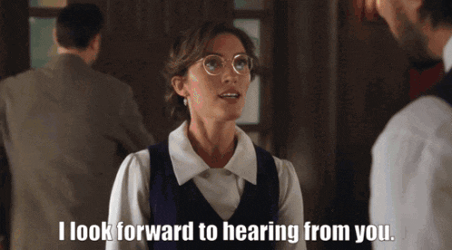 a woman wearing glasses is talking to a man and says " i look forward to hearing from you "