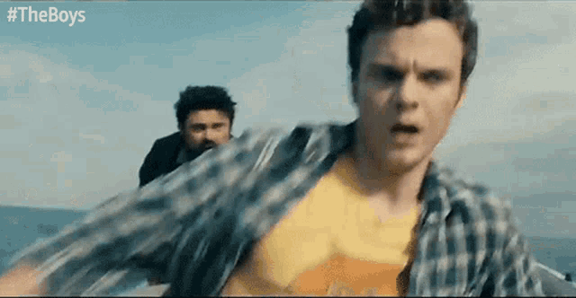 a man in a plaid shirt is running on a boat while another man watches .