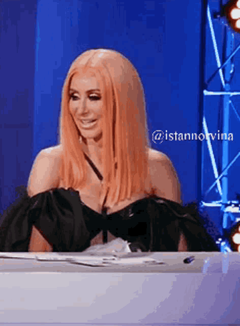 a woman with pink hair is sitting at a table and smiling .
