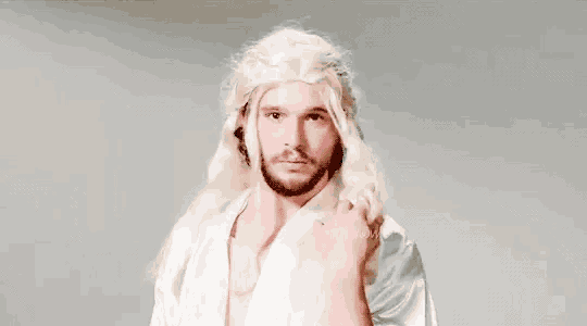 a man wearing a wig and a white robe is making a funny face .