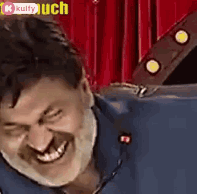 a man is making a funny face while sitting in front of a red curtain on a stage .