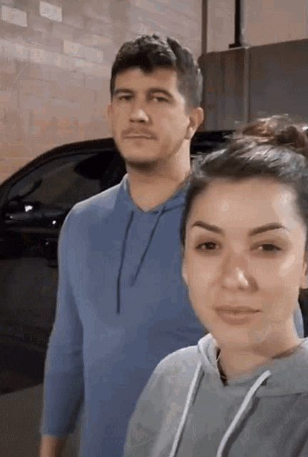 a man and woman are posing for a picture in front of a car .