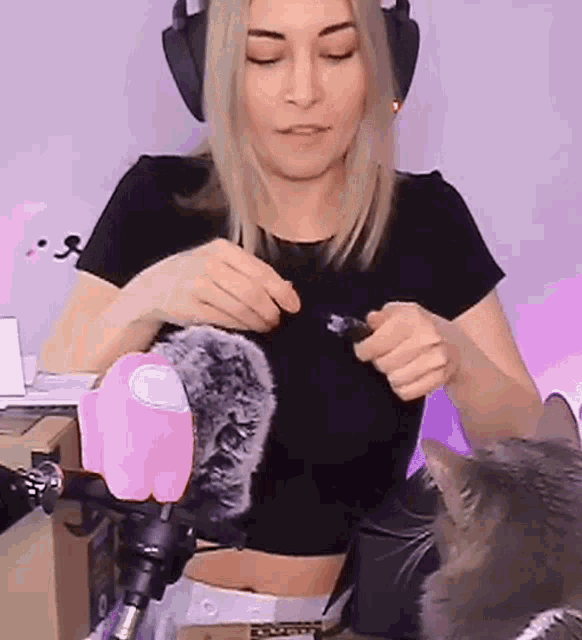a woman wearing headphones and a black crop top is playing with a cat .