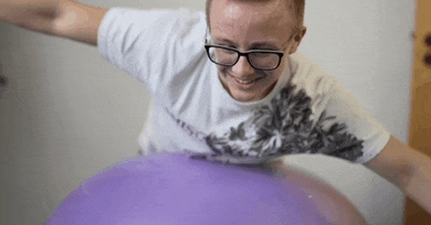 a young man wearing glasses and a white shirt is playing with a purple balloon .