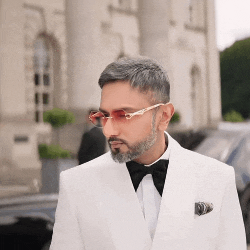 a man in a white suit and bow tie is wearing sunglasses and a pocket square