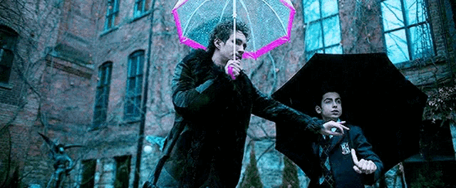 a man is holding a pink umbrella next to another man holding a black umbrella .