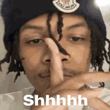 a man with dreadlocks is holding his finger to his mouth and making a shhh sign .