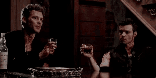 two men are sitting at a table with glasses of whiskey .