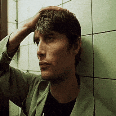 a man leaning against a wall holds his hand to his head