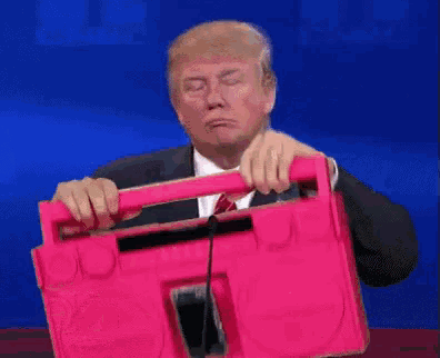 a man in a suit and tie is giving a speech in front of a pink box with chinese writing on it