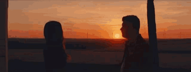 a man and a woman are standing next to each other at sunset .