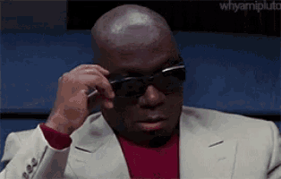 a bald man in a suit and sunglasses is adjusting his glasses .