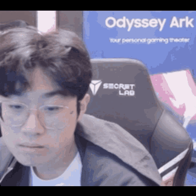 a man wearing glasses sits in front of an odyssey ark advertisement