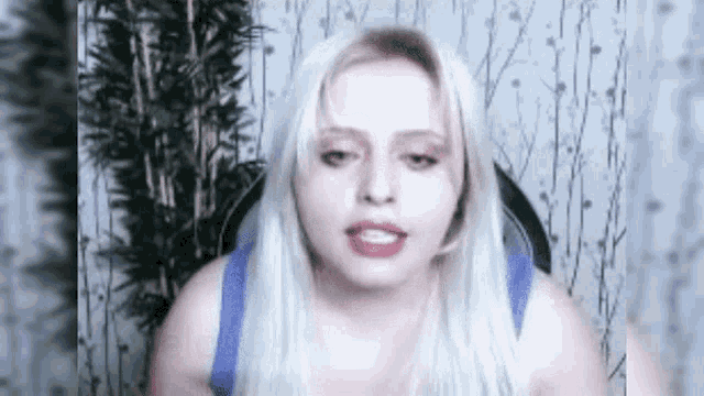 a woman with long blonde hair is sitting in a chair and talking to the camera .