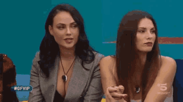 two women are sitting next to each other in front of a sign that says #gfvip on it