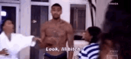 a man without a shirt is standing in front of a group of people and talking to them .