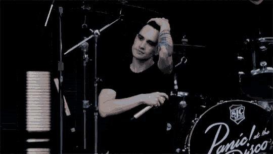 a man is singing into a microphone in front of a panic at the disco drum