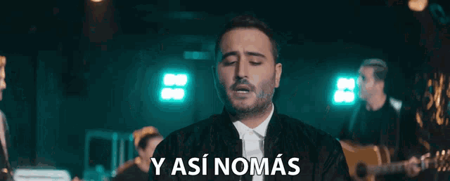 a man in a tuxedo is standing in front of a sign that says " y asi nomas "