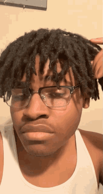 a man wearing glasses and a white tank top looks at the camera