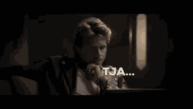 a man sitting in front of a laptop with the word tja written in white