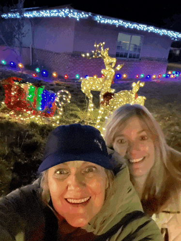 two women posing in front of a house with christmas lights