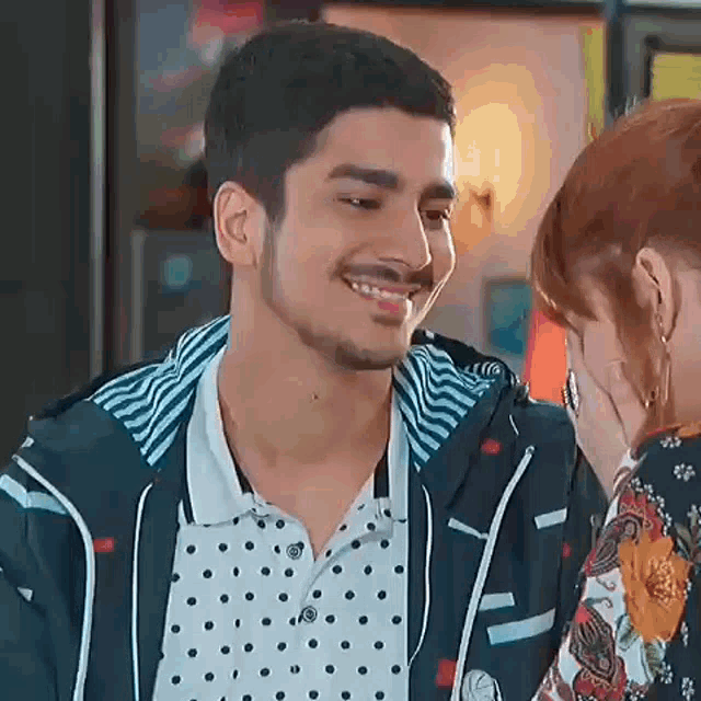 a man and a woman are looking at each other and smiling . the man is wearing a polka dot shirt .