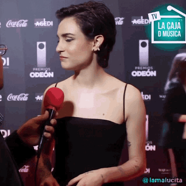 a woman in a black dress is being interviewed by a man on a red carpet sponsored by coca-cola